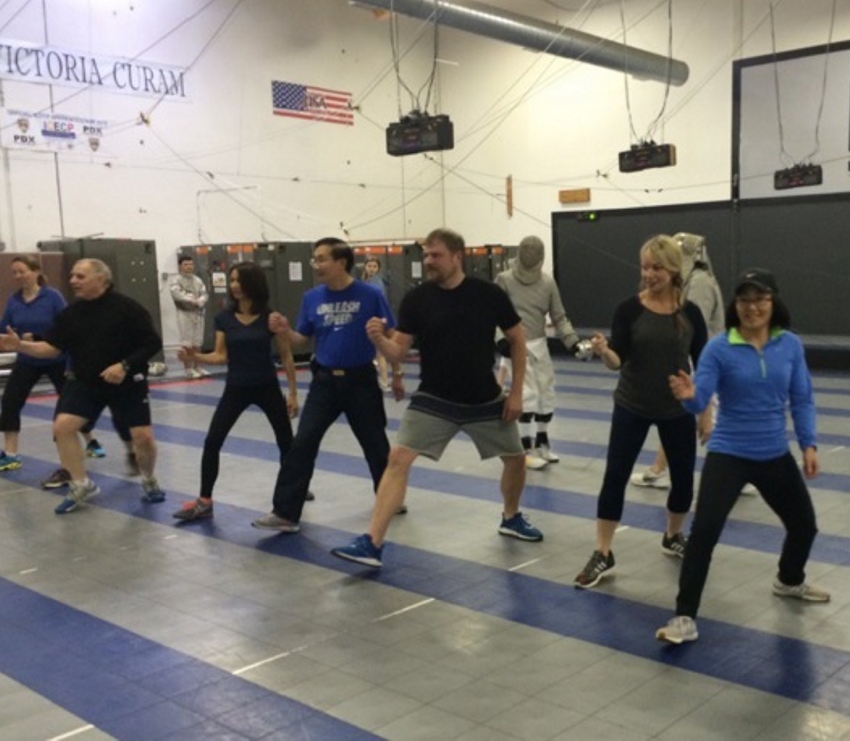 Group fencing class practicing footwork indoors.